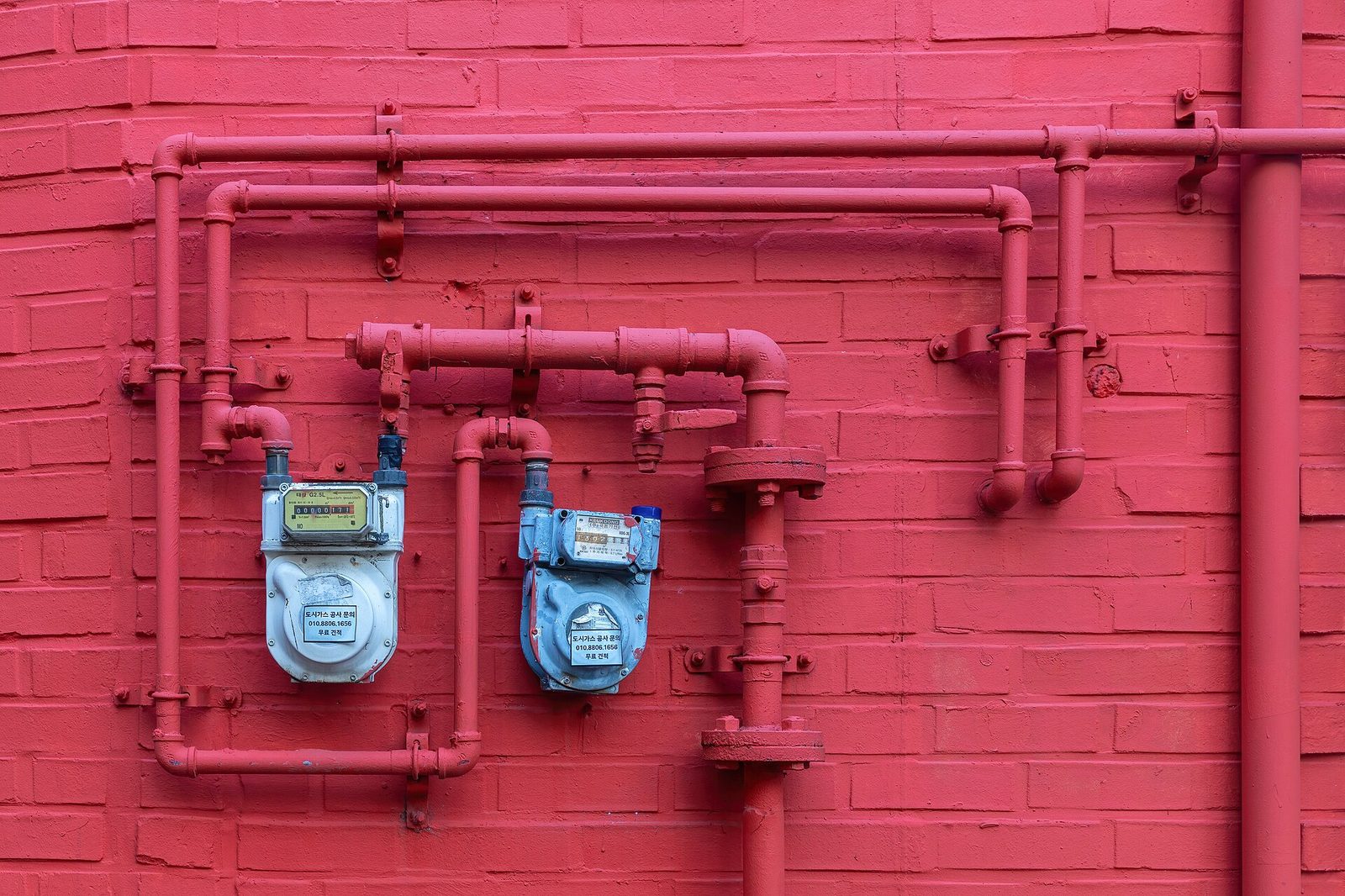 Two blue water meters mounted on a brick facade with pipes